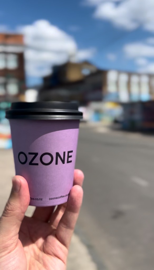 An Ozone takeaway coffee from HWK held up against street art and warehouses in Hackney Wick